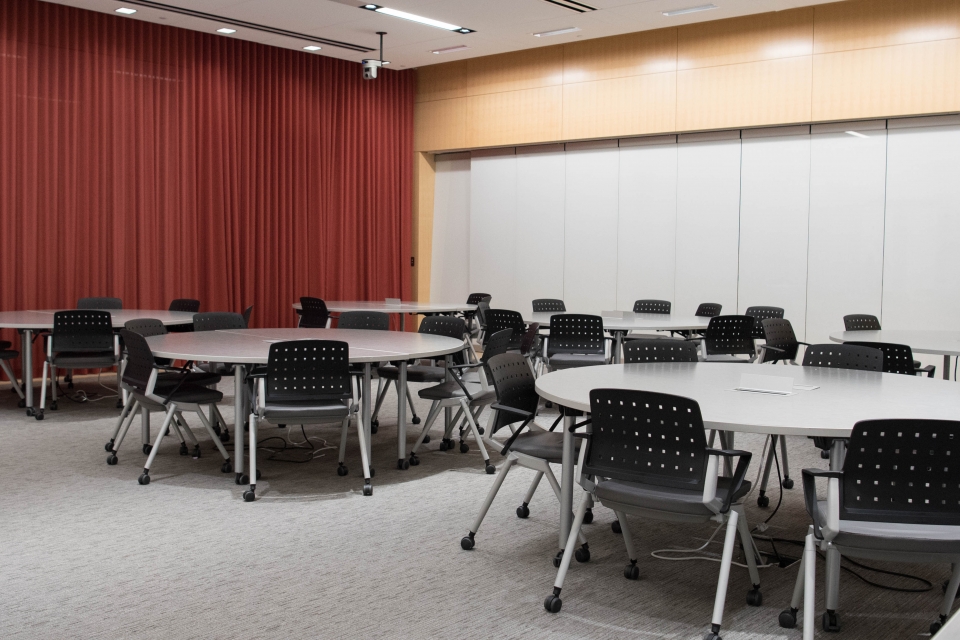 Classroom with round tables, chairs, and a red curtain backdrop