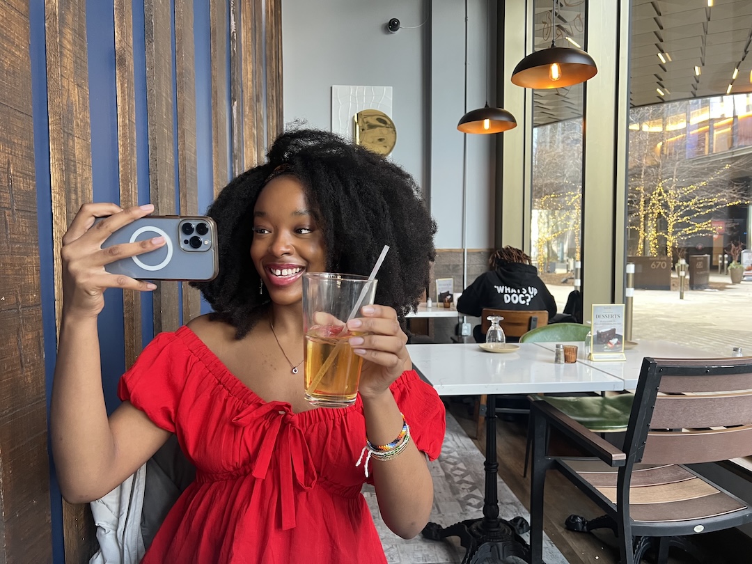 Ijeoma in a red dress with a drink in one hand and an iphone in the other