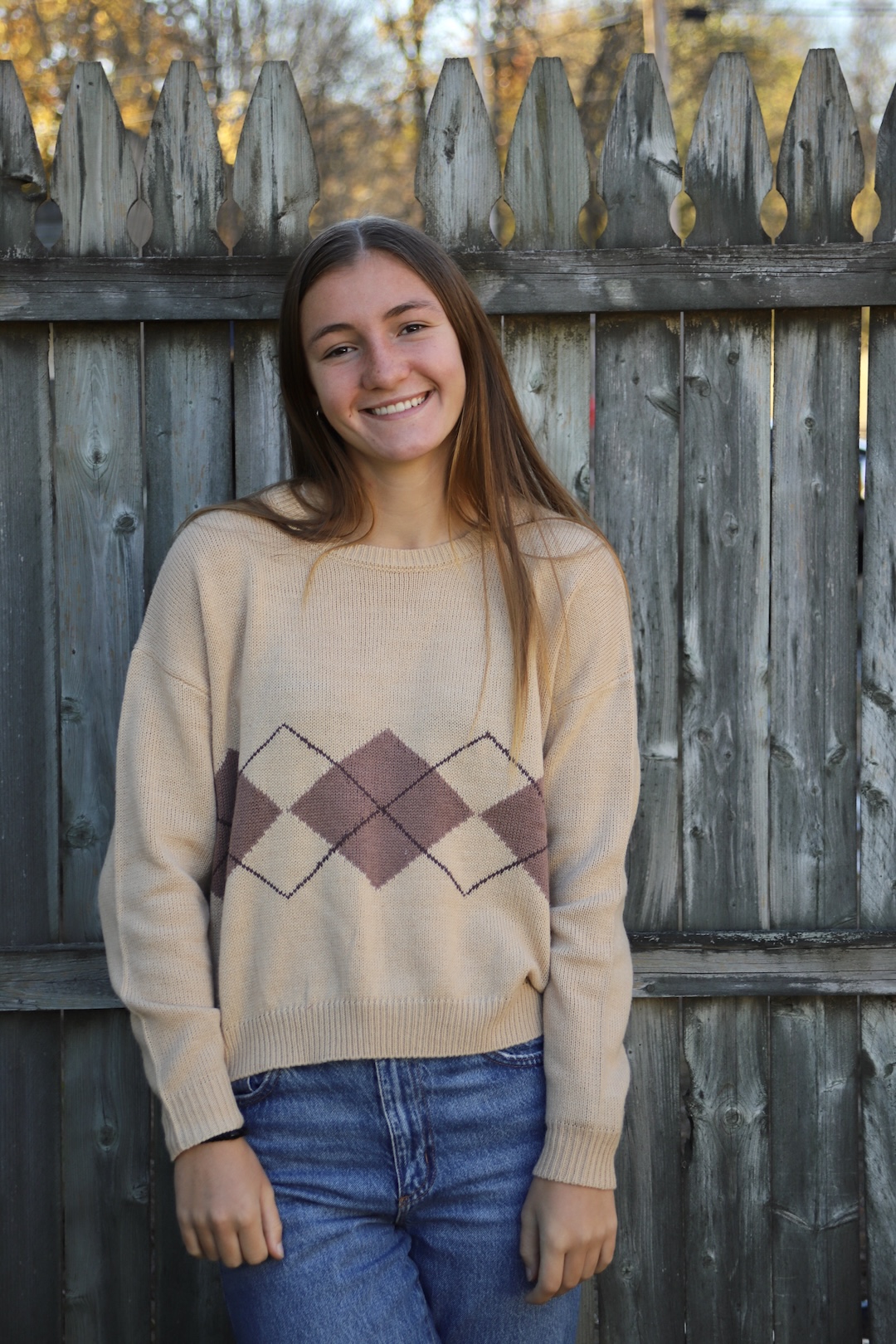 Sidney in a brown sweater standing in front of a fence