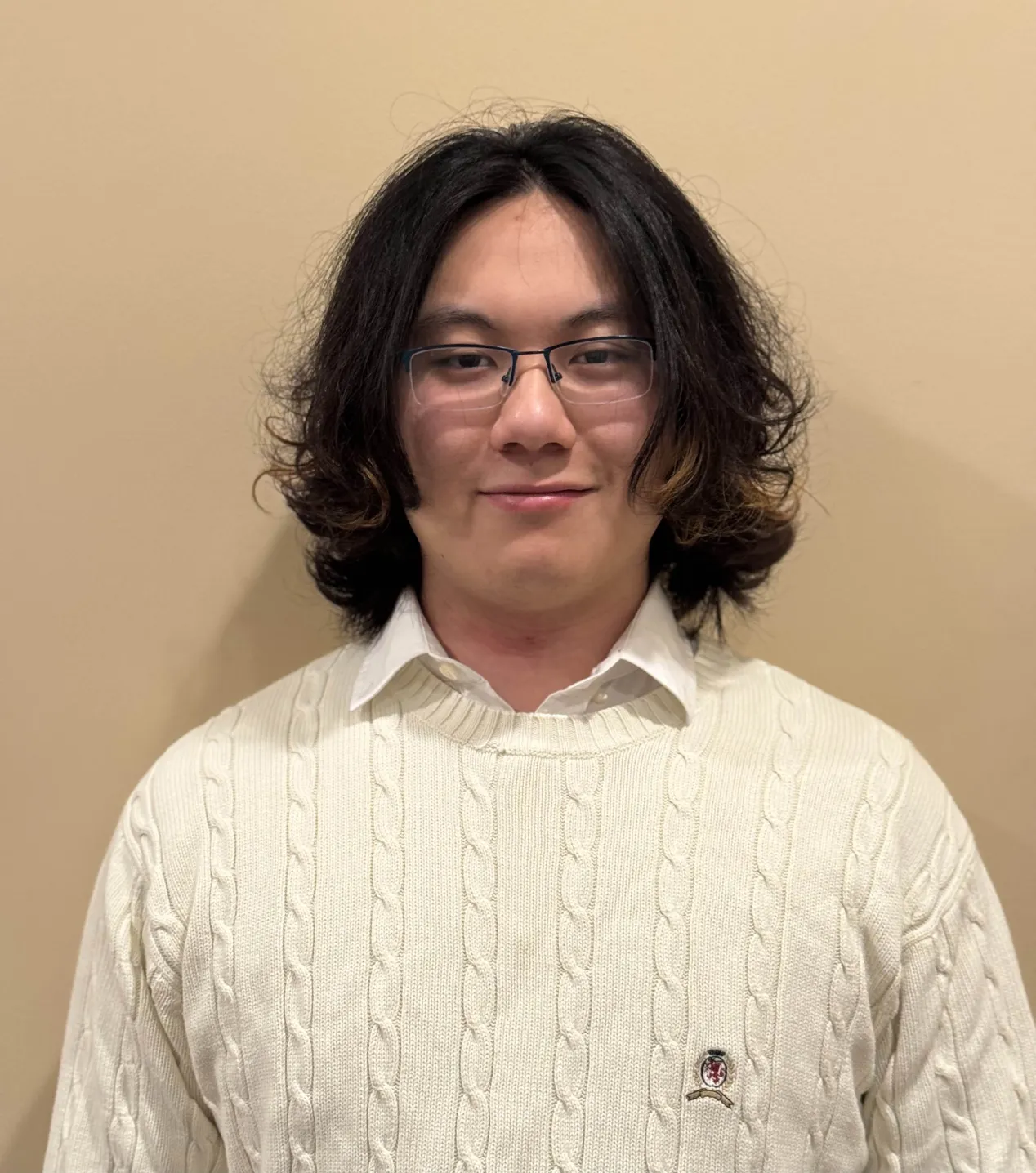 Student in a white sweater standing against a wall