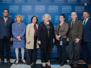 Moderator Dean Lach and panelists smiling with GW President Ellen Granberg