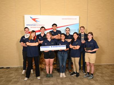 The 2023 GW Rocket Team smiling in front of a Spaceport America banner