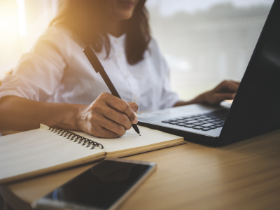 Woman writing at a desk with a computer