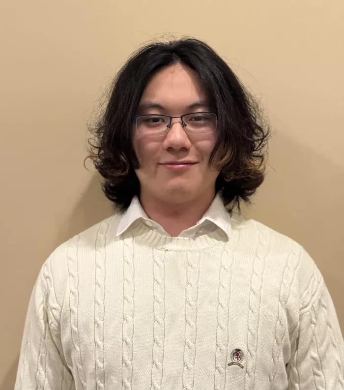 Student in a white sweater standing against a wall