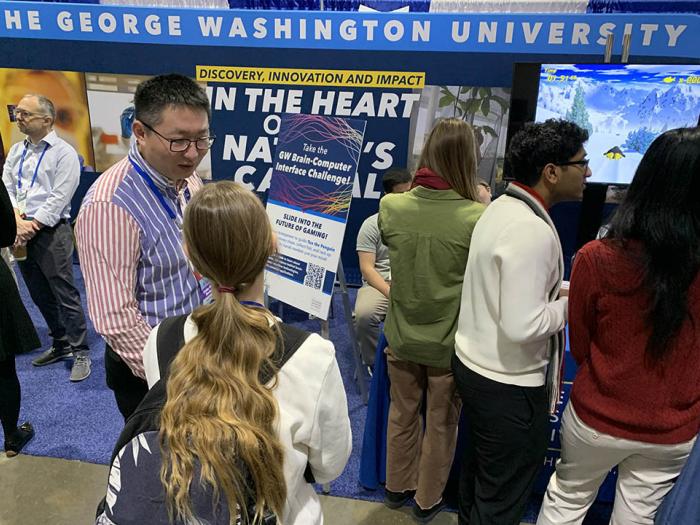 Computer Science Professor Xiaodong Qu (center) talks with visitors to GW’s booth at the 2025 AAAS annual meeting in Boston.